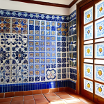 A richly detailed wall adorned with traditional Portuguese azulejos in a historic home's interior, such as a kitchen or hallway. Sunlight streams through a nearby window, highlighting intricate blue and white patterns alongside vibrant polychromatic scenes that evoke silent stories and a sense of timeless artistry. The space conveys a feeling of cool, inviting depth. Architectural photography style, high detail.